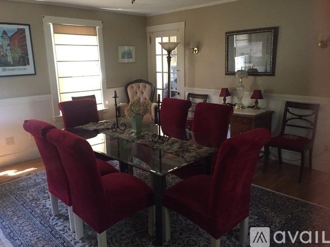 A dining room with a glass table and red chairs.