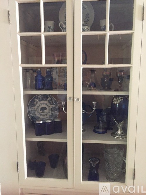 A white cabinet with glass doors is filled with various blue and white items.