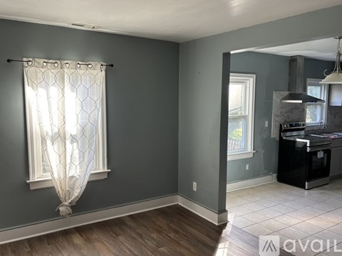 A room with a window covered by a sheer curtain and a kitchen area with a stove and oven.