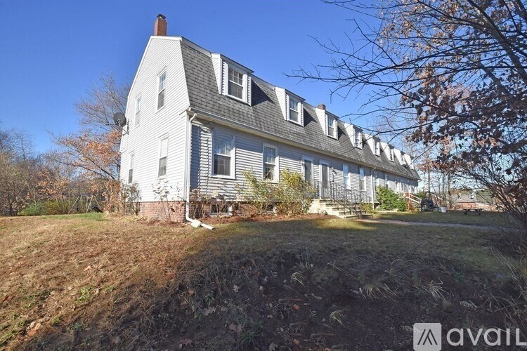 A white house with a black roof and a chimney is surrounded by grass and trees.