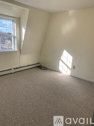 A room with a carpeted floor and a window letting in sunlight.