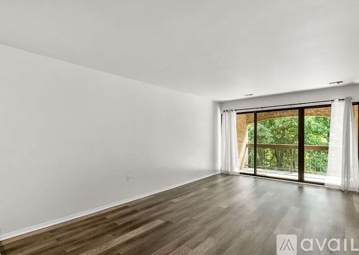 A room with wooden floors and a large window with a view of greenery outside.