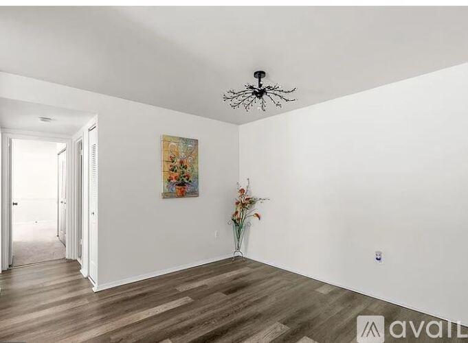 A room with a painting on the wall and a vase with flowers on the floor.