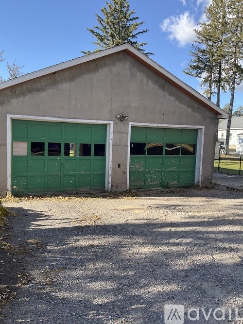 A two-door garage with green doors is in front of a tree.