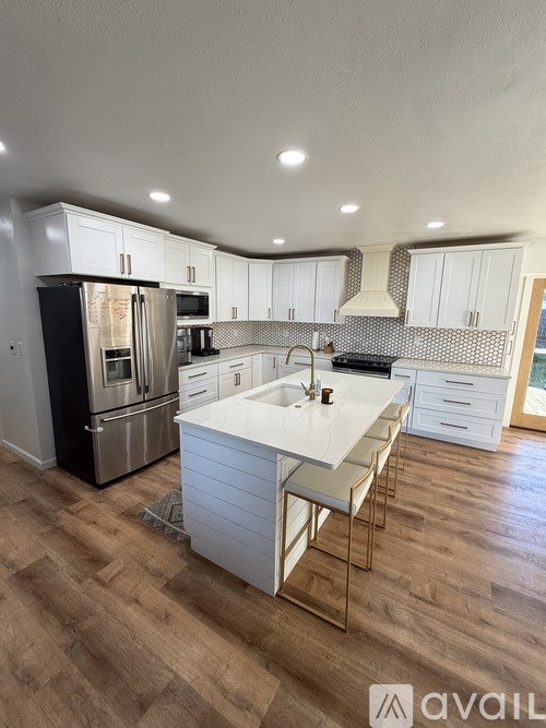 A kitchen with a black refrigerator, white cabinets, and a wooden floor.