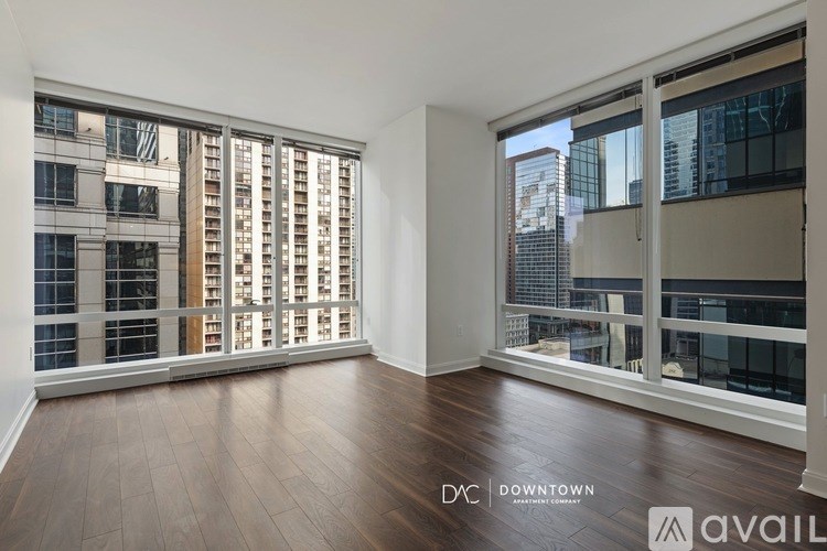 A spacious room with wooden floors and large windows overlooking a cityscape.