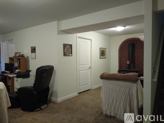 A room with a white door, a chair, a desk, and a small fireplace with a brick wall.