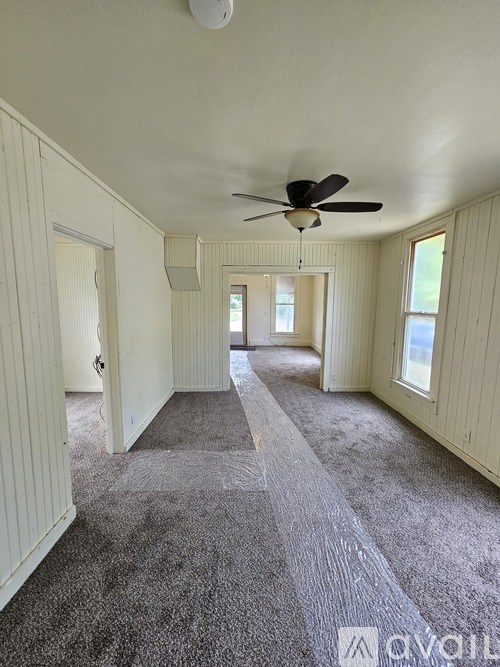 A long, empty room with a carpeted floor and a ceiling fan.