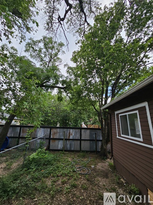A backyard with a brown house, a fence, and trees.