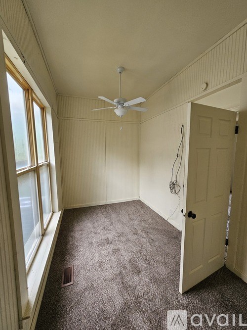 A room with a carpeted floor, a ceiling fan, and a door.
