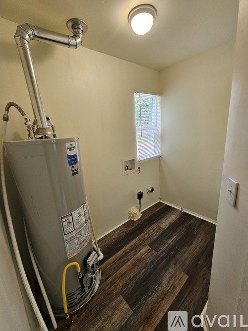 A water heater is installed in a room with wooden flooring and white walls.