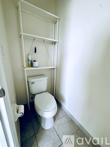 A white toilet in a small bathroom with a shelf above it.