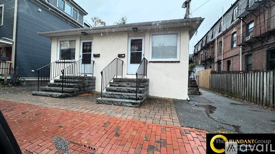 A small white house with a black metal staircase leading to the front door.