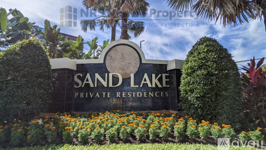 A sign for Sand Lake Private Residences is surrounded by greenery and flowers.