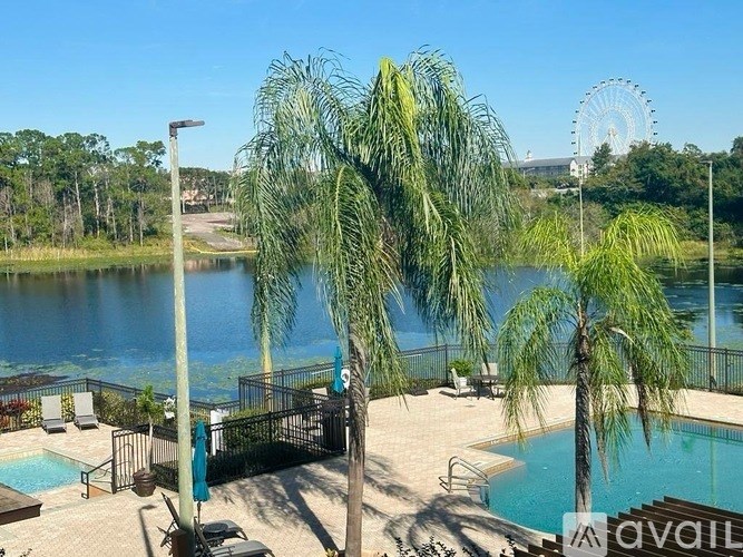 A pool area with a view of a lake and a Ferris wheel in the distance.