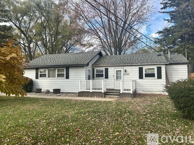A house with a grey roof and white siding is surrounded by a grassy area with fallen leaves.