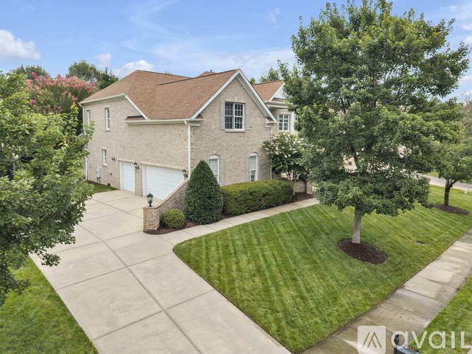 A house with a brown roof and a white garage door is surrounded by a well-manicured lawn and trees.