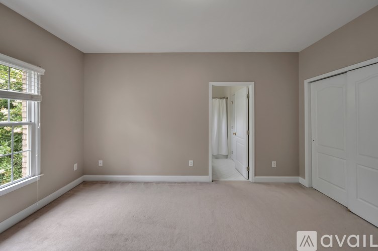 A room with beige walls and carpeting, a window with a view of trees, and a white door.