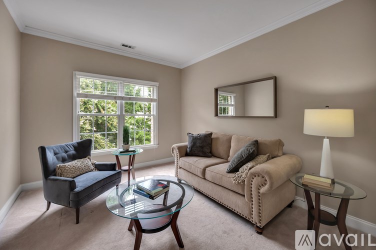 A living room with a black chair, a beige couch, and a glass coffee table.
