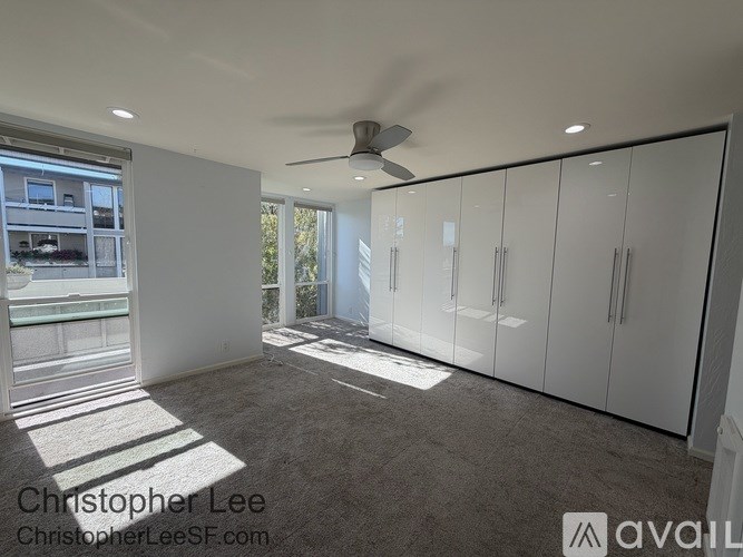 A room with a ceiling fan and a large window with sunlight coming through.