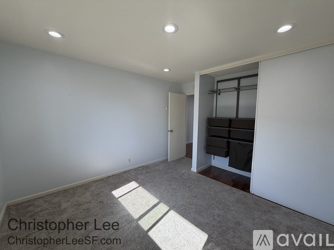 A room with white walls and a grey carpet with a white door on the right side.