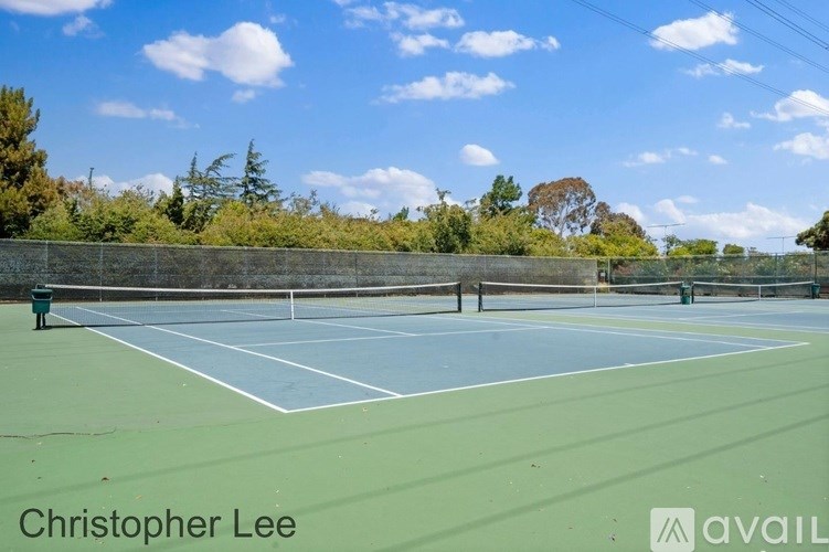A tennis court with a green fence and trees in the background.