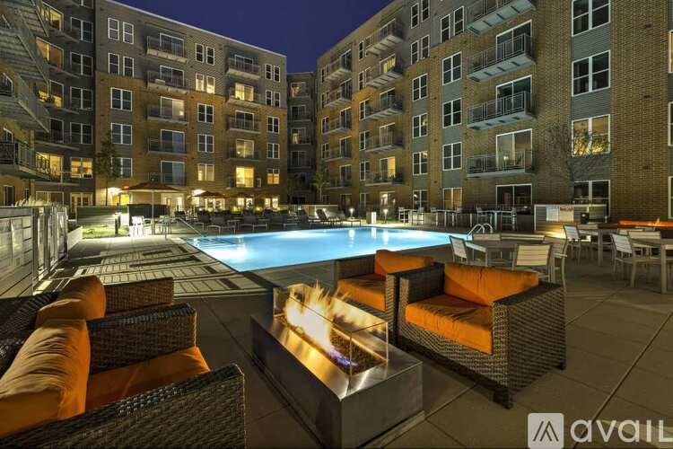 A pool surrounded by chairs and a lit fire pit at night.