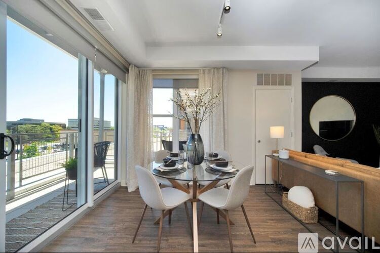 A modern dining room with a glass table and chairs, a balcony with a view of the city, and a black and white decorated wall.