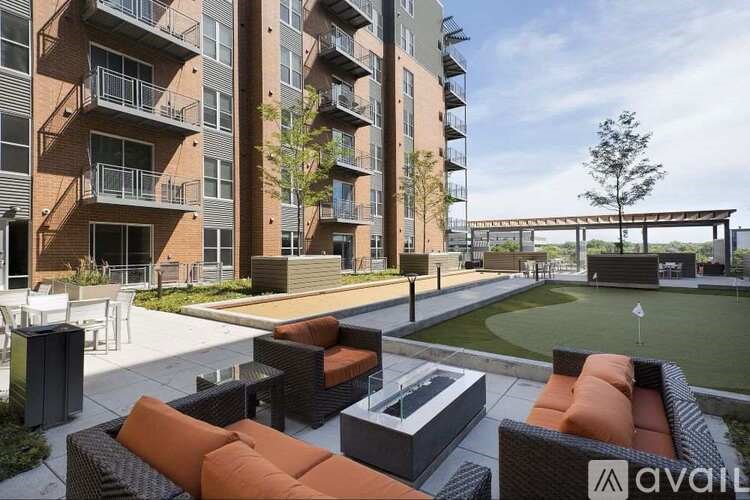A modern outdoor seating area with orange couches and a fire pit in front of a multi-story apartment building.
