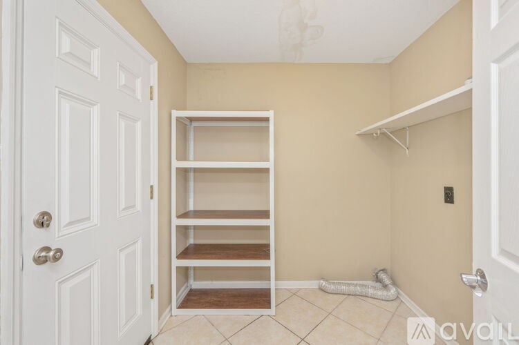 A white door is on the left of a room with a shelf and a white wall.