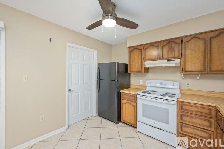 A kitchen with a black refrigerator, white stove, and wooden cabinets.