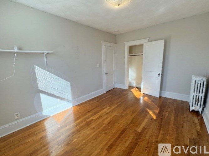 A room with wooden flooring and white walls, with a door and a window.