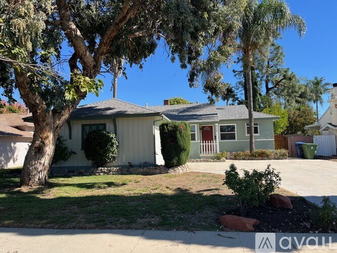 A house with a red door is surrounded by trees and bushes.