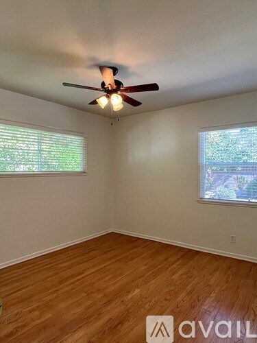 A room with a ceiling fan and two windows.
