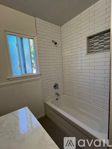 A white tiled bathroom with a window and a bathtub.