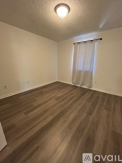 A room with wooden flooring and a window with curtains.