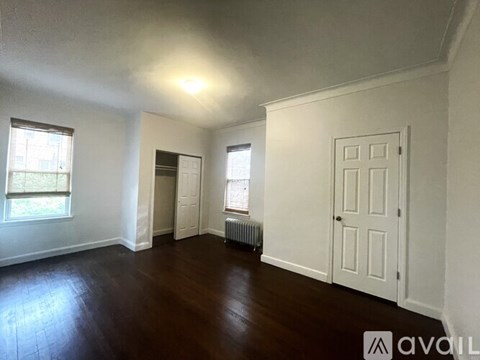 A room with wooden floors and white walls, with a window and a door visible.