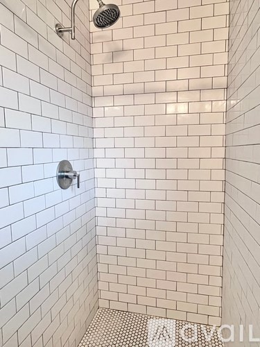 A white tiled shower with a silver shower head.