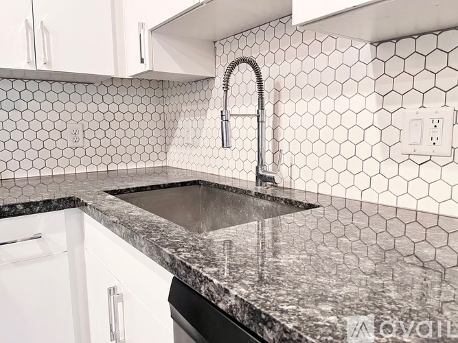 A kitchen with a black granite countertop and white hexagonal tiles.