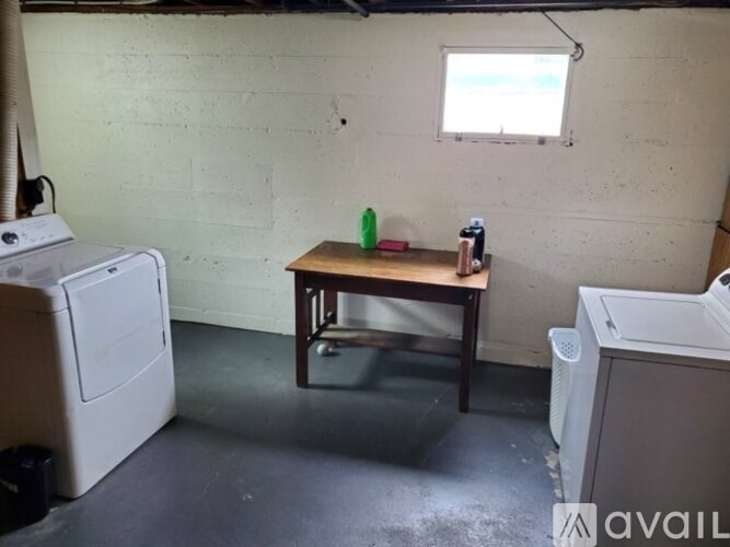 A room with a washing machine, a table with a green bottle and a window.