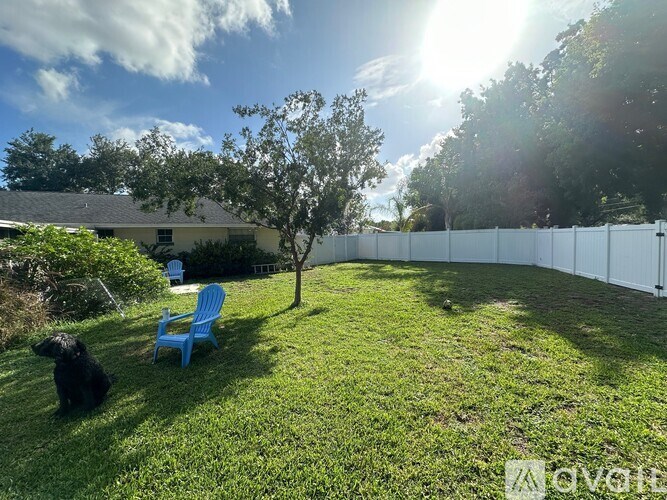 A black dog sits on a lawn next to a blue chair.