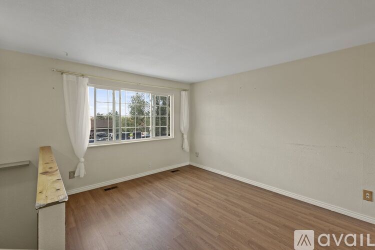A room with wooden flooring and a window with white curtains.