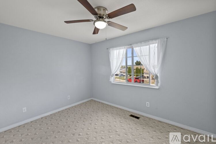 A room with a ceiling fan and a window with curtains.