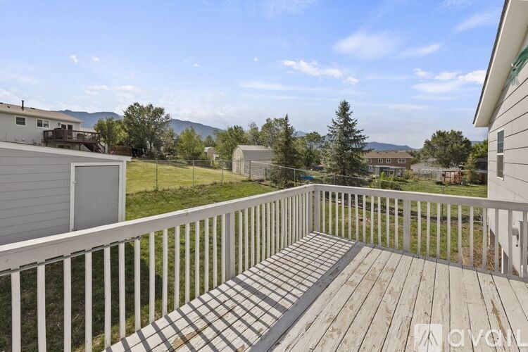 A wooden deck with a white railing overlooks a grassy area with trees and houses in the distance.