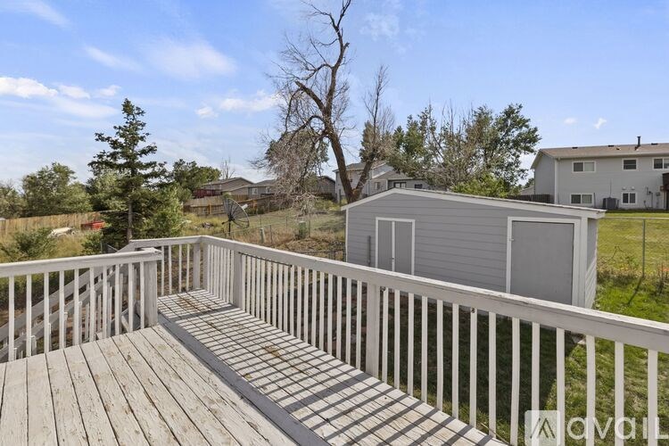 A deck with a white railing and a grey shed in the background.