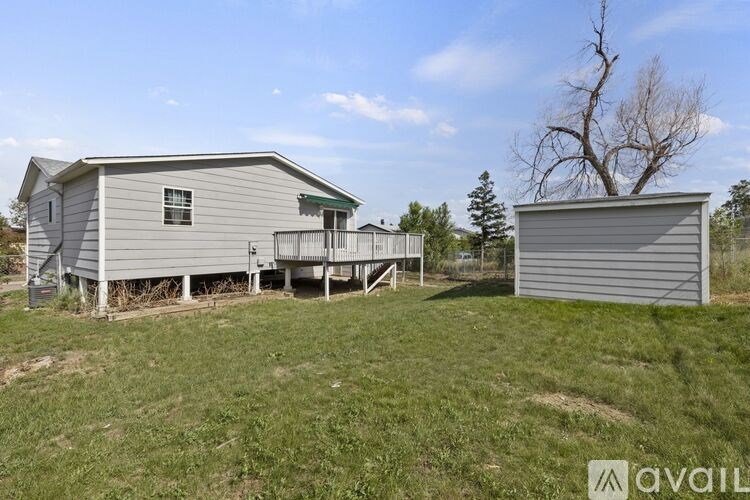 A house with a grey siding and a green roof is surrounded by a grassy area with a tree and a shed.
