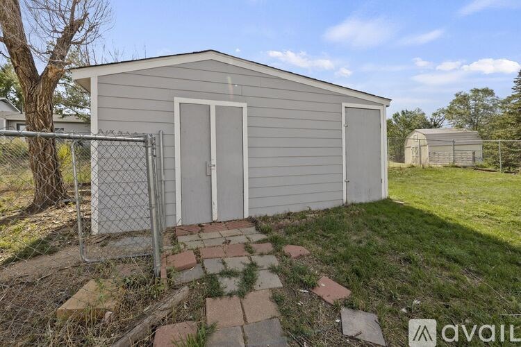A grey shed with a white door and a metal fence.