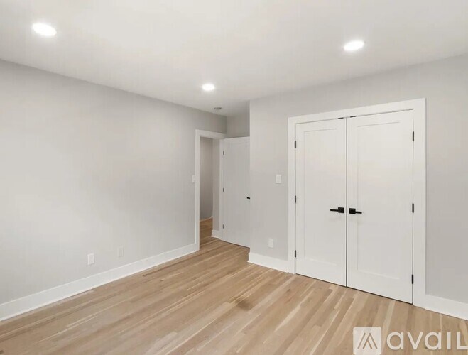 A room with white walls and wooden flooring, featuring a large white door and a smaller doorway.
