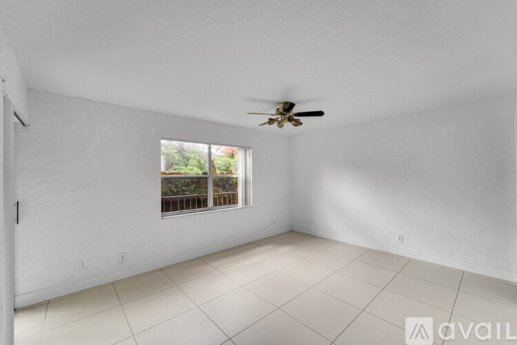 A room with a ceiling fan and a window overlooking a balcony.