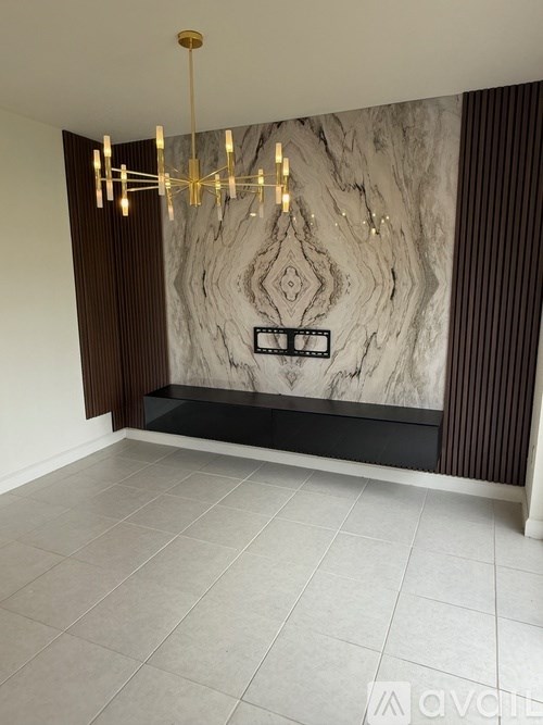 A modern chandelier hangs over a marble wall in a spacious room.